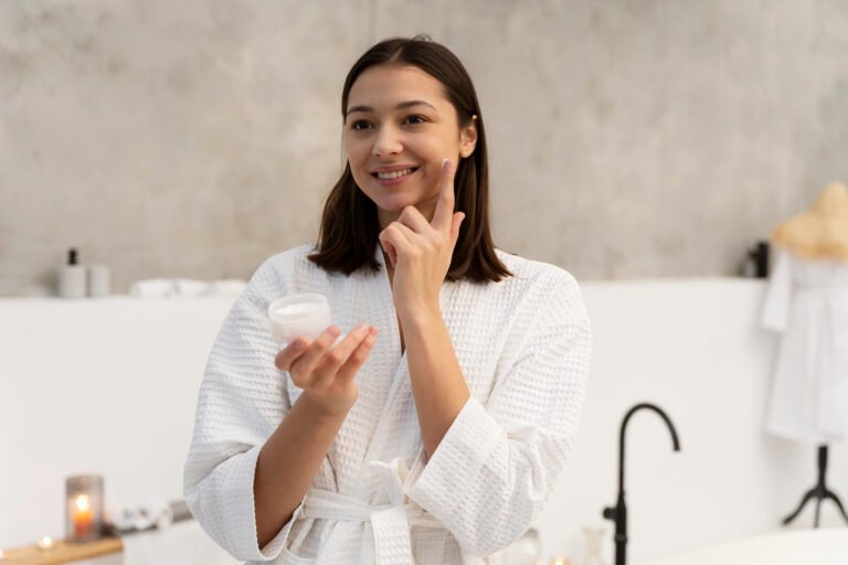 Woman applying science-backed skincare serum to face following dermatologist-approved routine with vitamin C and moisturizer on bathroom counter
